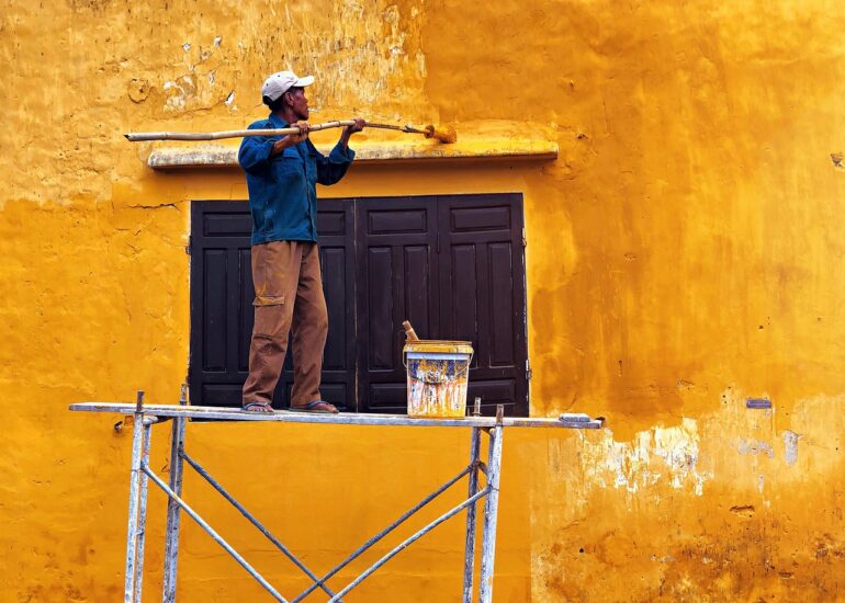 Man die muur verft met gele verf op een wankele steiger