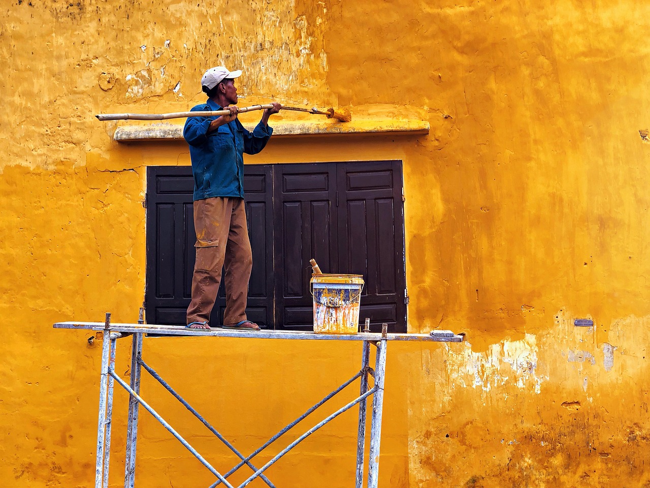 Man die muur verft met gele verf op een wankele steiger